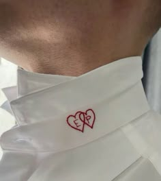 a close up of a person wearing a white shirt with two hearts on the collar