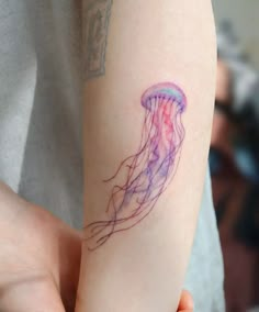 a person with a tattoo on their arm holding a jellyfish in the air,