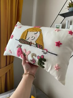 a woman is holding up a pillow with embroidered designs on it and she has her hand on the pillow