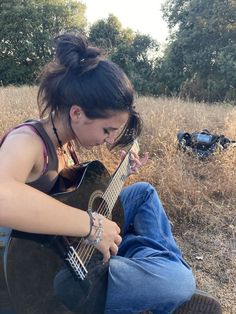 a woman sitting on the ground playing an acoustic guitar