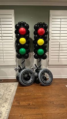 two traffic lights made out of balloons in front of white shutters and wood flooring