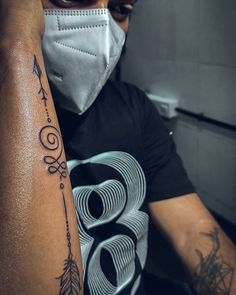 a man wearing a mask and holding his arm up to his face with an arrow tattoo on it