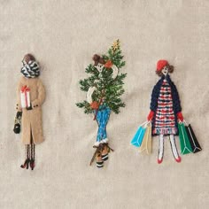 three handmade christmas ornaments are displayed on a white cloth background, with small trees in the middle