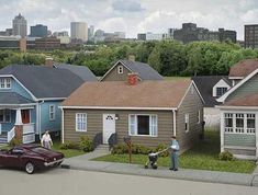 two men mowing the grass in front of some small houses on a city street