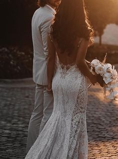 a bride and groom are standing together on the cobblestone road at sunset in their wedding attire