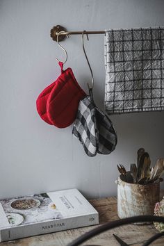 a pair of oven mitts hanging from a hook next to a cookbook on a wooden table