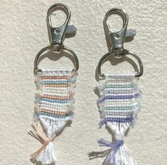 two crocheted keychains with tassels hanging from hooks on a wall