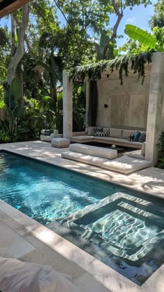 an outdoor swimming pool surrounded by greenery and stone patio with seating area on the other side