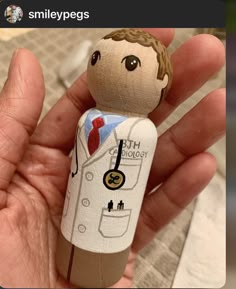 a hand holding a small wooden doll with a doctor's coat and tie on