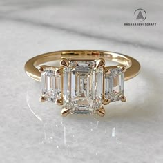 a three stone diamond ring sitting on top of a white counter with gold trimming