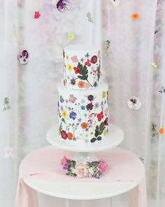 a three tiered cake with flowers on it sitting on top of a white table