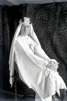 an old black and white photo of a man in a nun outfit sitting on a chair