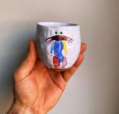 a hand holding a painted cup in front of a white wall