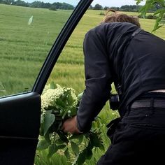 a man is looking out the window of a car at an open field with flowers