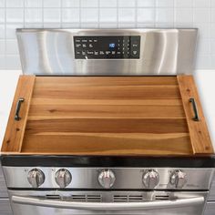 a stainless steel stove with wooden cutting board on top