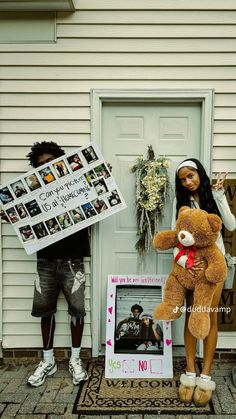 two people standing in front of a house with a large teddy bear holding a sign