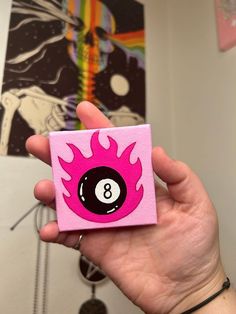 a person holding up a pink and black eight ball pin with flames on the front