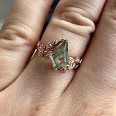 a close up of a person's hand wearing a ring with an emerald stone