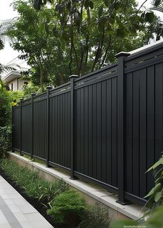 a long black fence next to a lush green garden