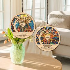 two stained glass ornaments hanging from chains on a table next to a vase with flowers