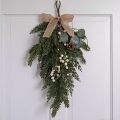 a wreath hanging on the front door with pine cones, berries and evergreens attached to it