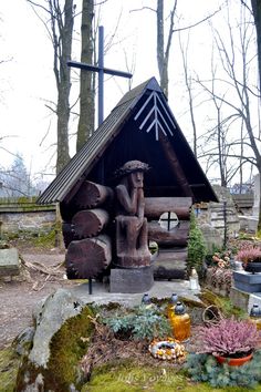 a wooden statue sitting in front of a log cabin with a cross on it's roof