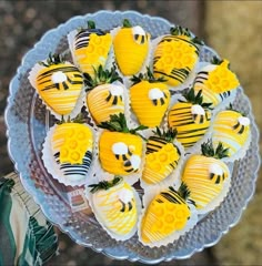 there are many yellow and black decorated strawberries on the platter with green leaves