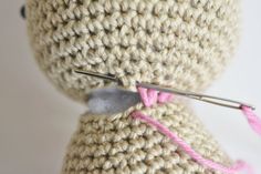 a crocheted teddy bear with pink thread on it's back and needles in its mouth