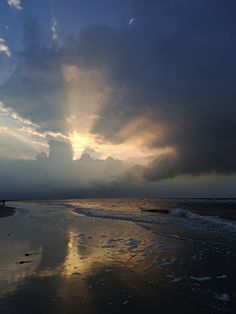 the sun is setting over the ocean with clouds in the sky and people walking on the beach