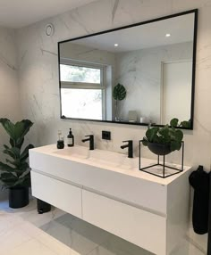 a white bathroom with a large mirror above the sink and plants on the counter top