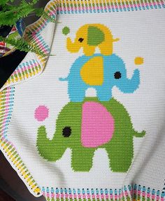 a cross - stitch baby blanket with an elephant on it and a potted plant in the background