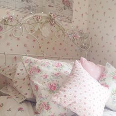 a white bed topped with lots of pillows next to a wooden headboard covered in pink flowers