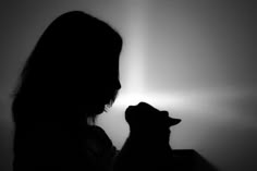 the silhouette of a woman holding a cat in her arms and looking up at it