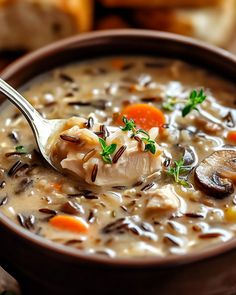 a close up of a spoon in a bowl of soup with mushrooms and carrots