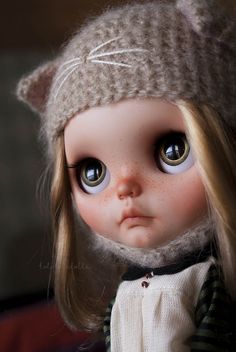 a close up of a doll wearing a knitted hat and dress with cat ears