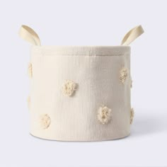 a white knitted basket with pom - poms on the sides and two wooden handles