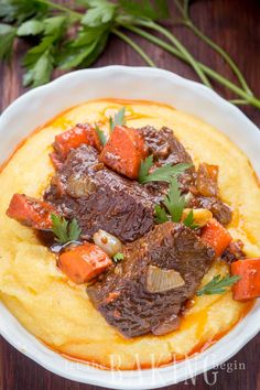 a white bowl filled with meat and vegetables on top of polenta mashed potatoes