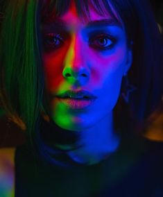 a woman with bright lights on her face and neck is looking at the camera while standing in front of a neon colored background