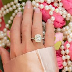 a close up of a person's hand with a ring and flowers in the background