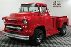 an old red pick up truck is parked in a room with black and white checkered flooring