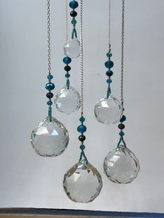 three clear glass beads hanging from chains on a white wall with blue and black beading