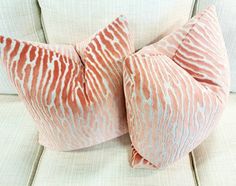 two pillows on the back of a couch with an orange and white pattern in it