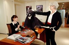 two women in business attire standing around a desk with an object on it's arm