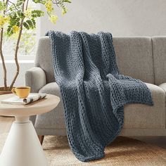 a gray couch with a blue knitted blanket on top of it next to a coffee table