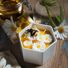 a bee sitting on top of a bowl filled with liquid and daisies next to a jar of honey