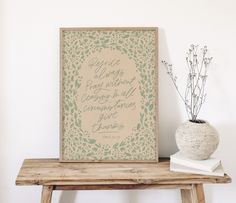 a wooden table topped with a vase filled with flowers next to a framed quote on the wall