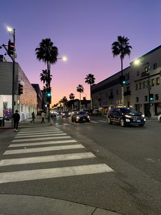 cars are driving down the street at dusk with palm trees in the background and people walking on the sidewalk