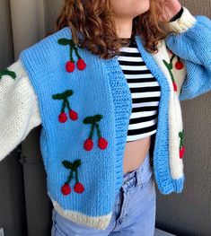 a woman wearing a blue sweater with cherries on it and holding her hand up to her face