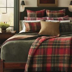 a bed with plaid comforter and pillows in a bedroom next to a painting on the wall