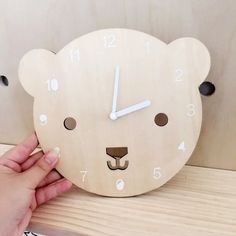 a wooden clock with a bear's face and numbers on the face is being held up by a hand